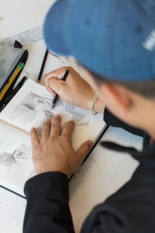 Student is drawing in a small notebook.