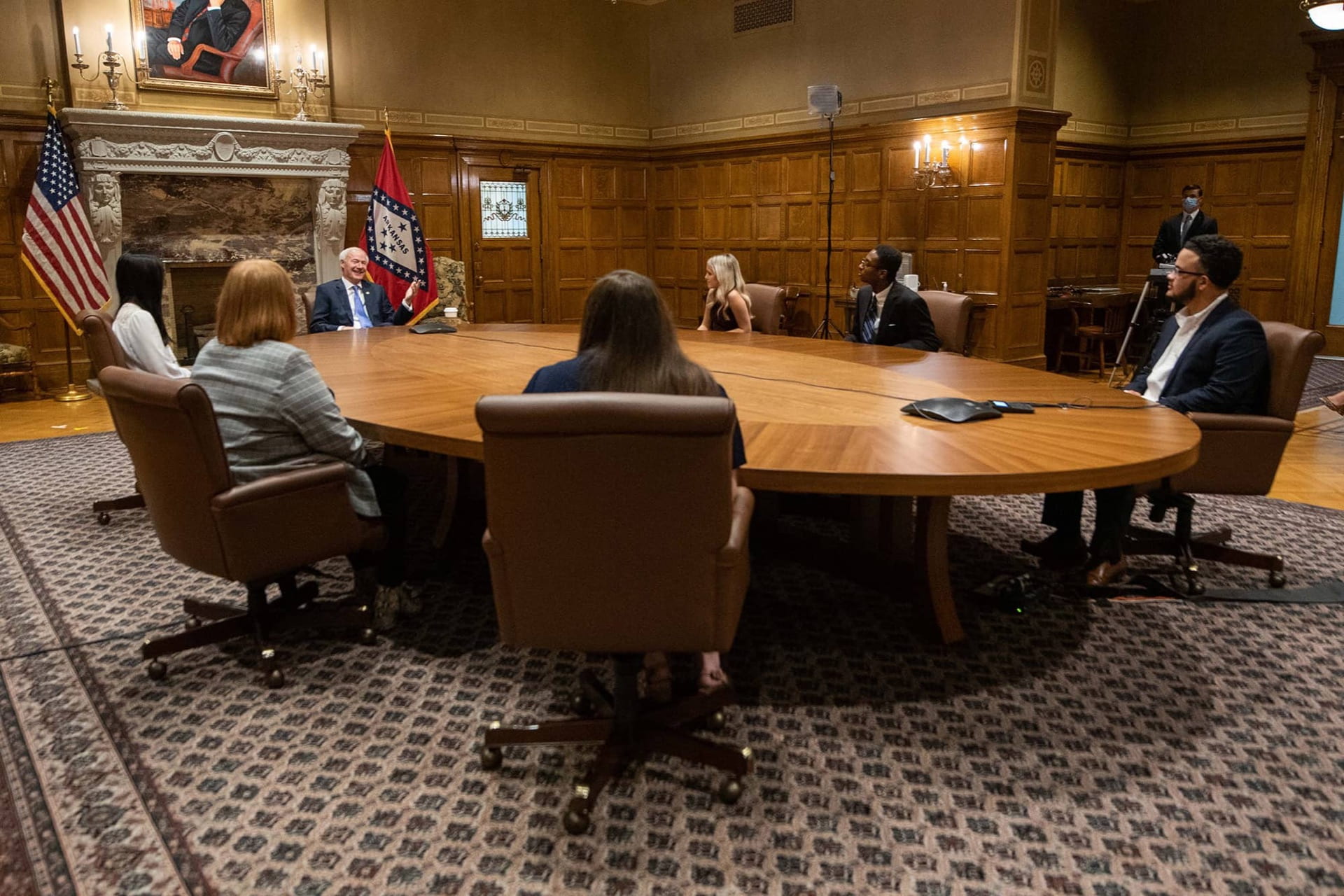 6 college students are seated around a large table headed by Arkansas Gov. Asa Hutchinson. 