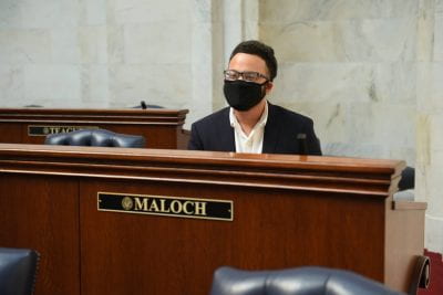 Masked student is seated behind a lecturn. 
