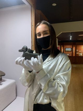 Female student wearing mask and gloves carefully cradles a figurine.