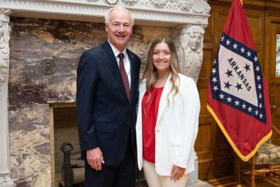 Madison and Gov. Hutchinson pose, with a brick wall and an Arkansas flag behind them.