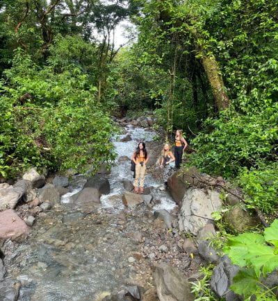 three women students crossing a stream 