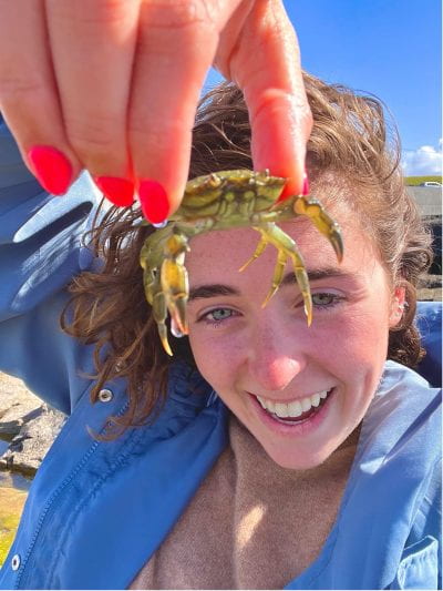 A woman holding a small crab up to the camera 
