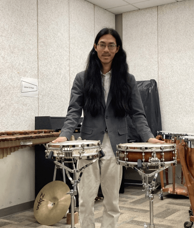 Student Yoshio behind two snare drums in a music room 