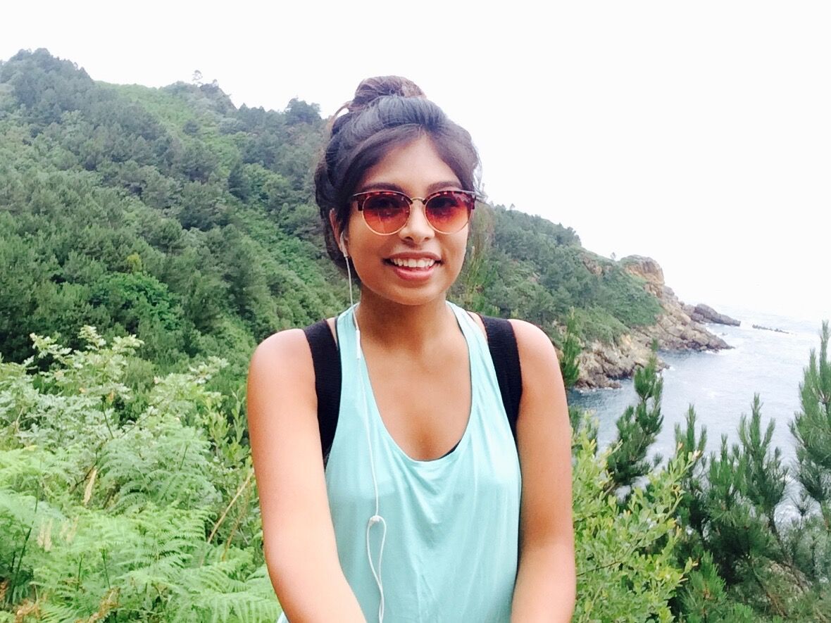 Young woman with sunglasses and backpack, pictured in coastal area.