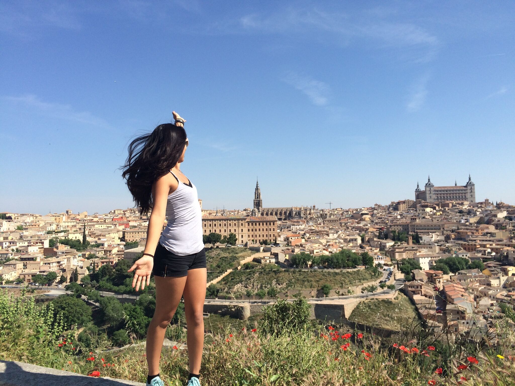 Photo of young woman gesturing towards historic Spanish city. 