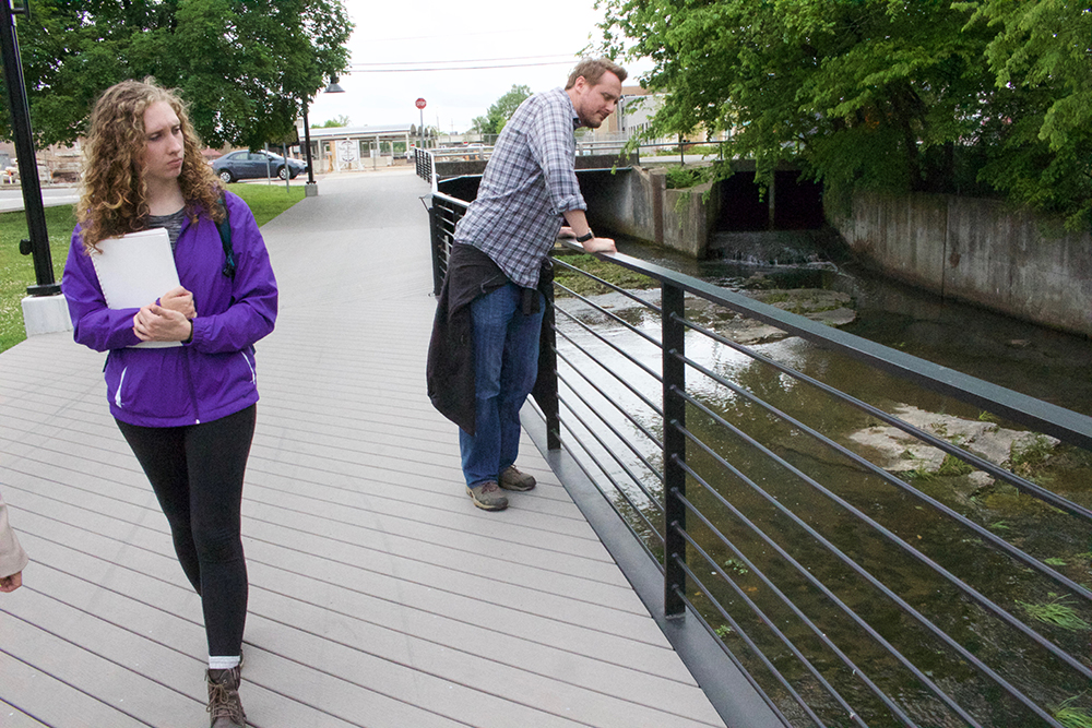 Professor and student examine a creek that runs through downtown. 