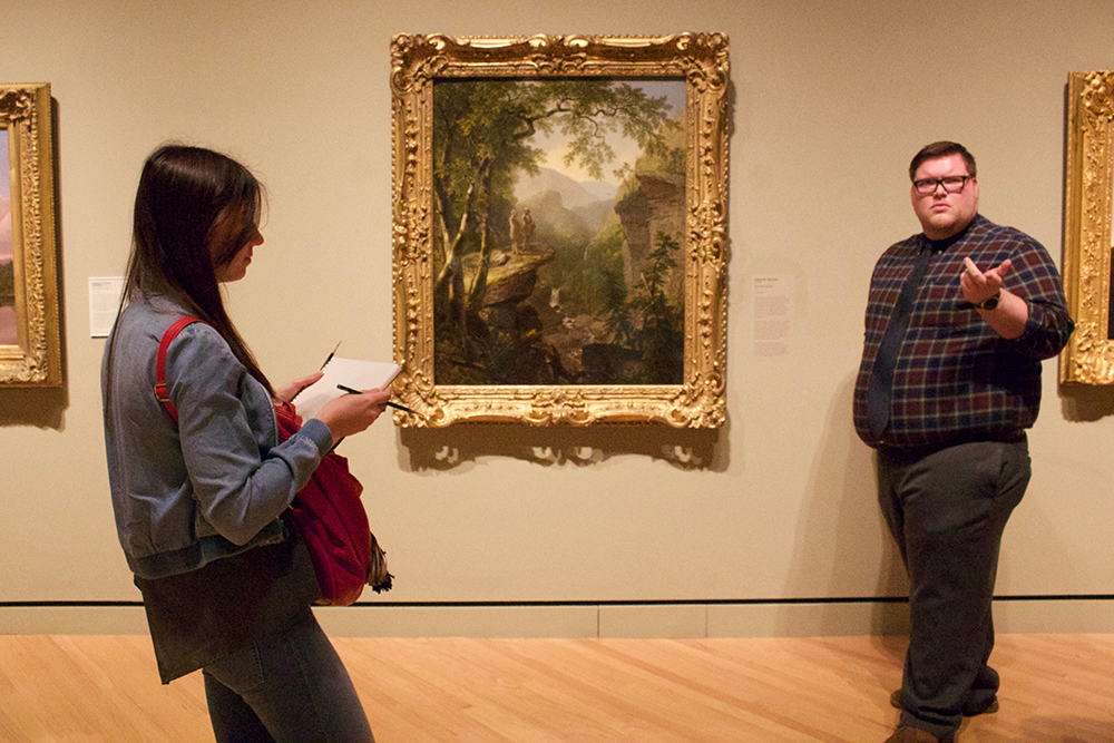 Docent discusses landscape painting while student sketches. 