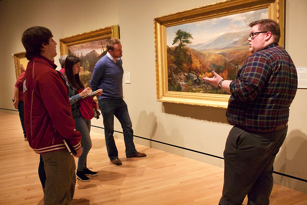 Professor, students and docent examine another landscape painting. 