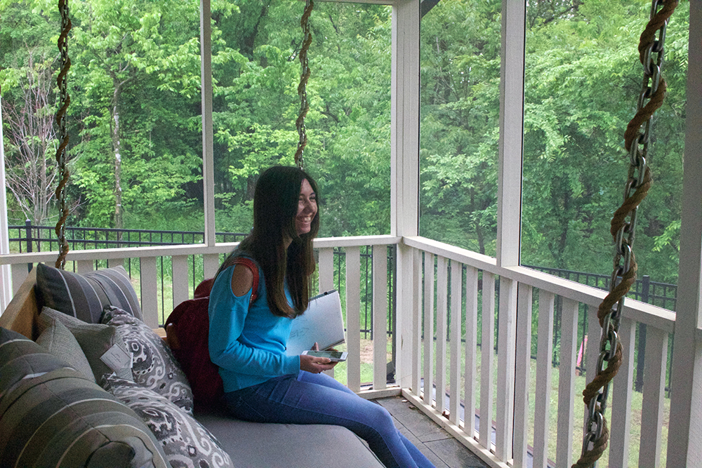 Student sits on a porch swing installed on a screened porch. 