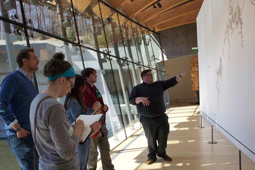 Professor, students and docent examine a sculpture installation. 